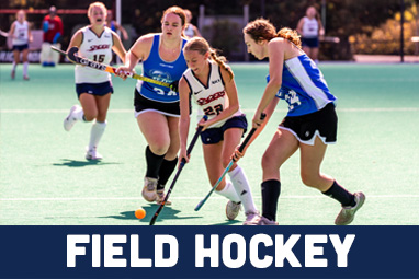 A University of Richmond Field Hockey Player dribbling in between 2 opposing players.